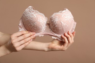 Photo of Woman holding lace bra on dark beige background, closeup