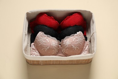 Photo of Beautiful bras in basket on beige background, above view