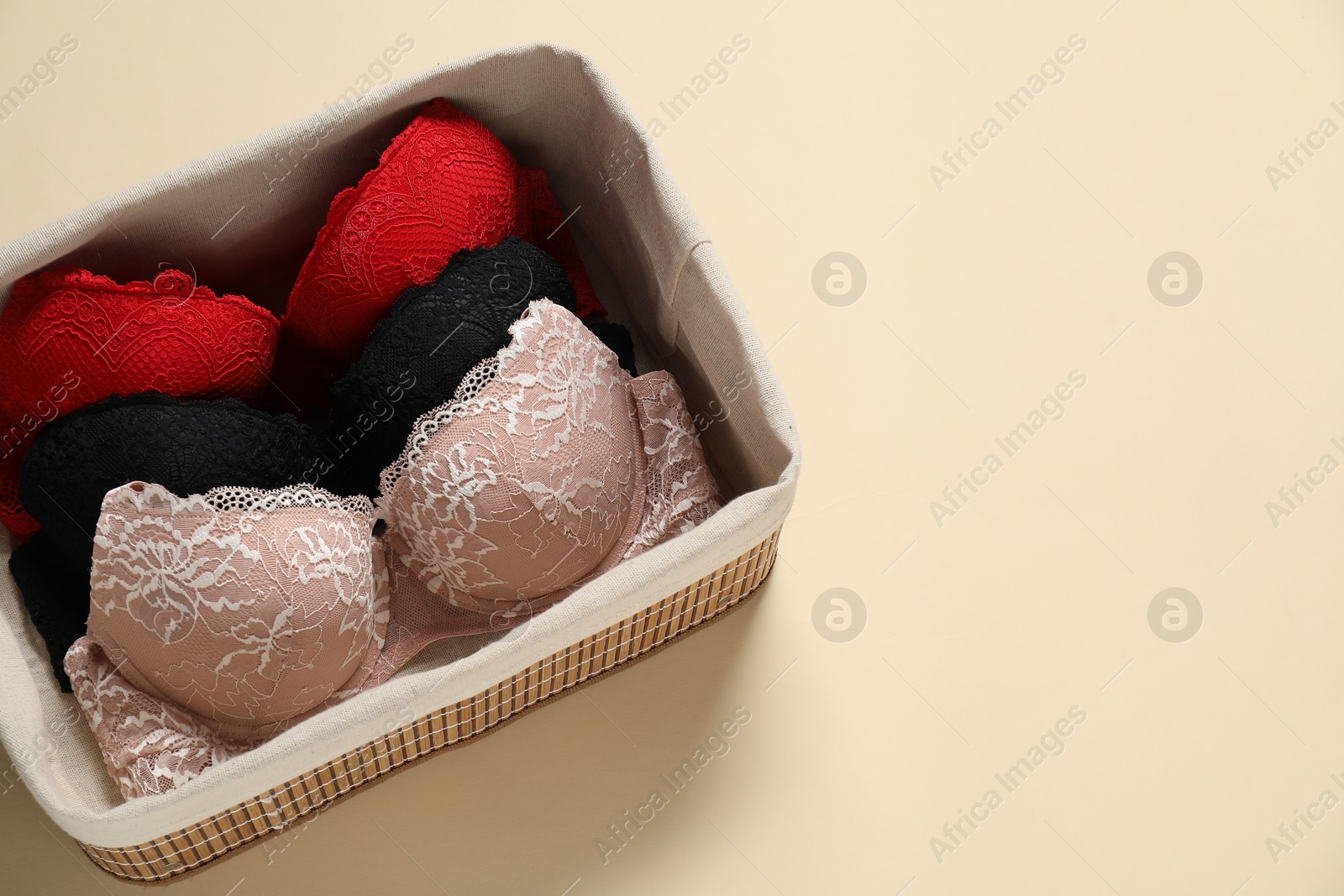 Photo of Beautiful bras in basket on beige background, top view. Space for text