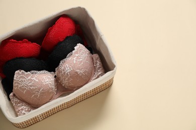 Photo of Beautiful bras in basket on beige background, top view. Space for text