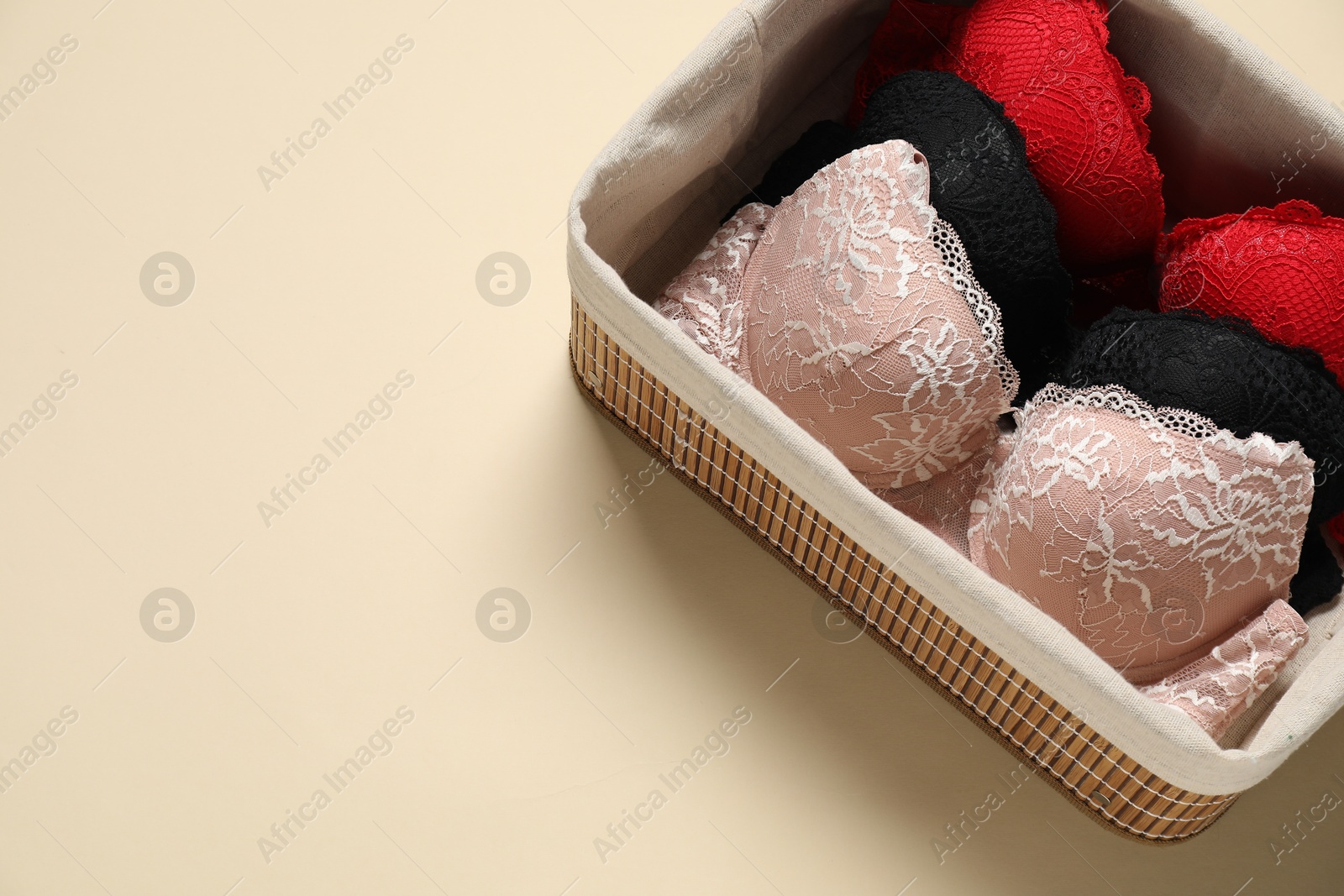 Photo of Beautiful bras in basket on beige background, above view. Space for text