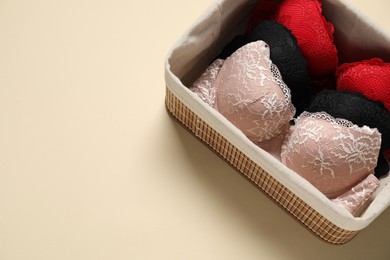 Photo of Beautiful bras in basket on beige background, above view. Space for text