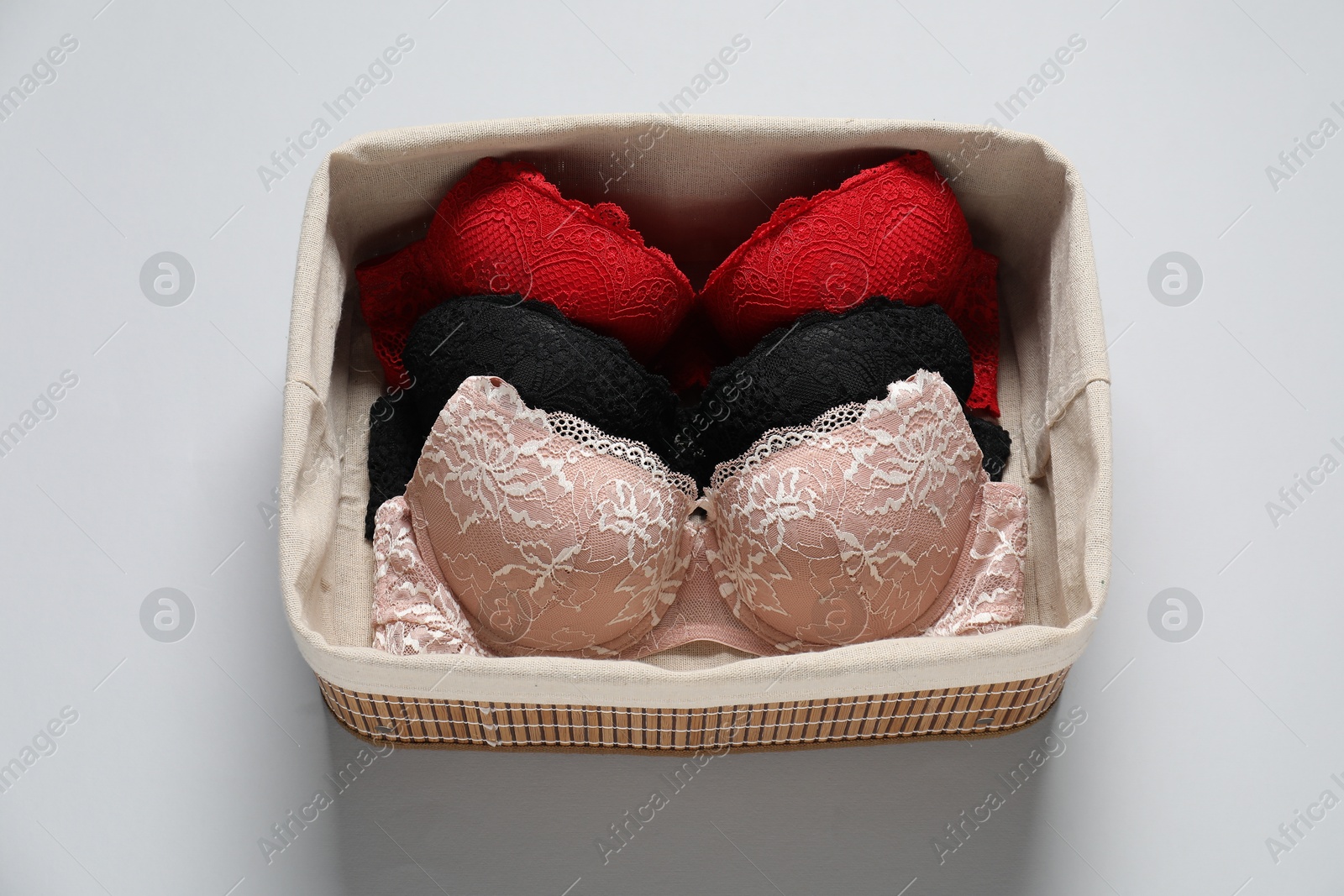 Photo of Beautiful bras in basket on light background, above view