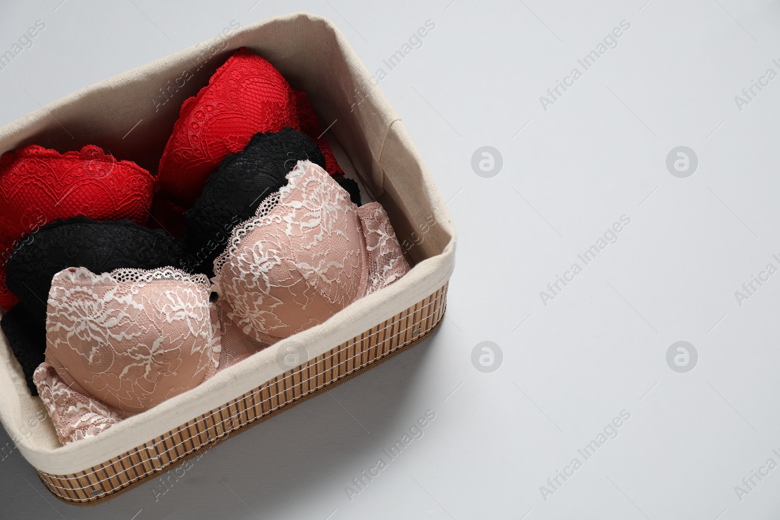 Photo of Beautiful bras in basket on light background, above view. Space for text