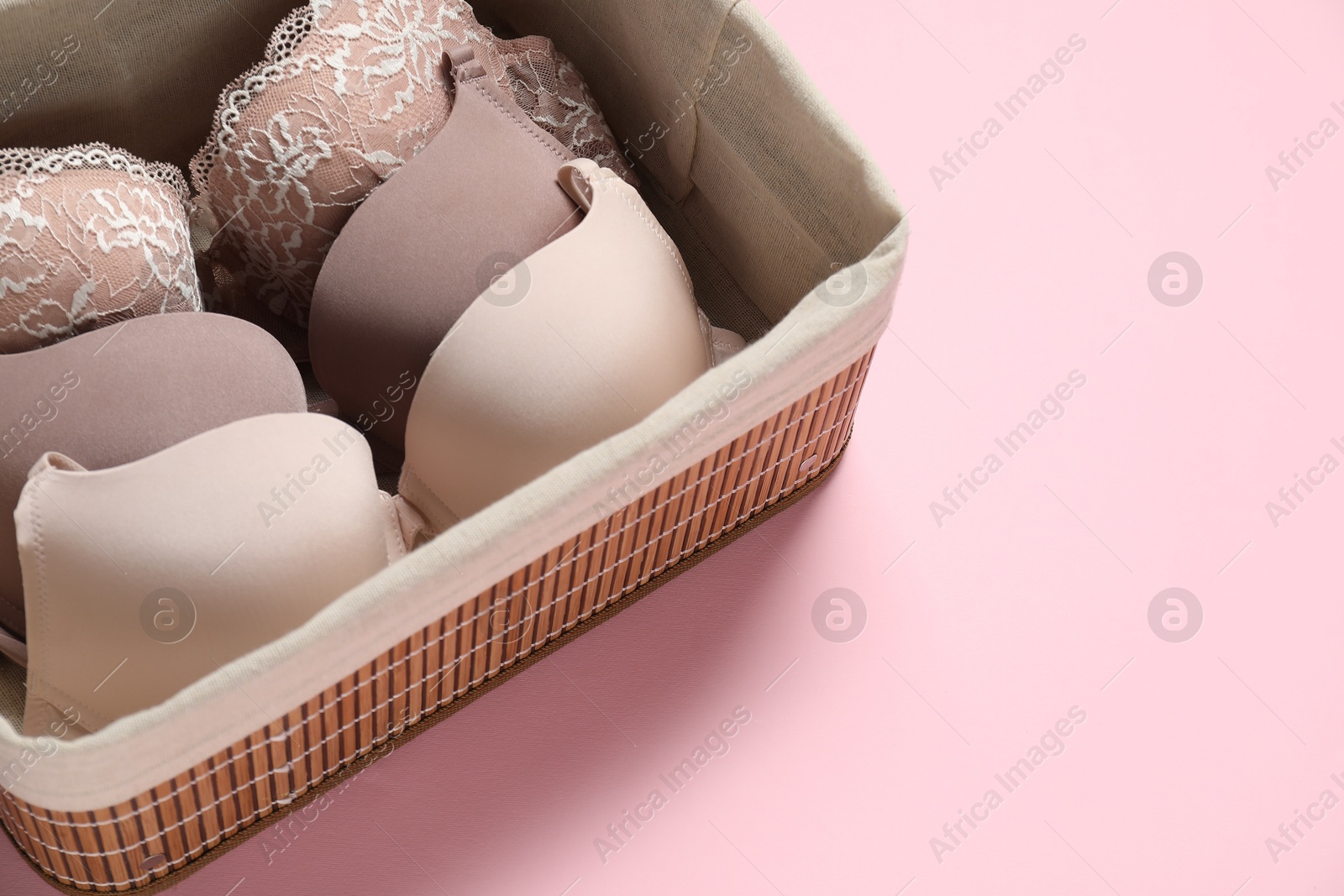 Photo of Beautiful bras in basket on pink background, closeup. Space for text