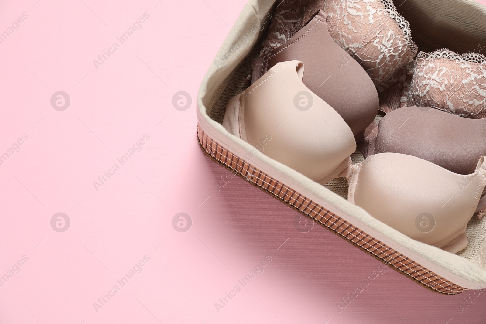 Photo of Beautiful bras in basket on pink background, top view. Space for text