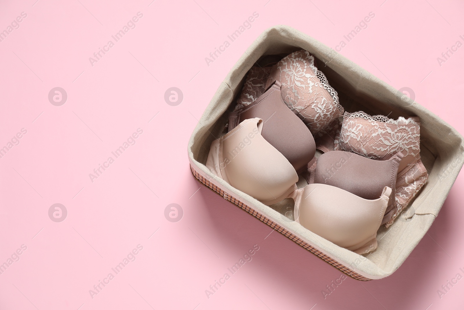 Photo of Beautiful bras in basket on pink background, top view. Space for text