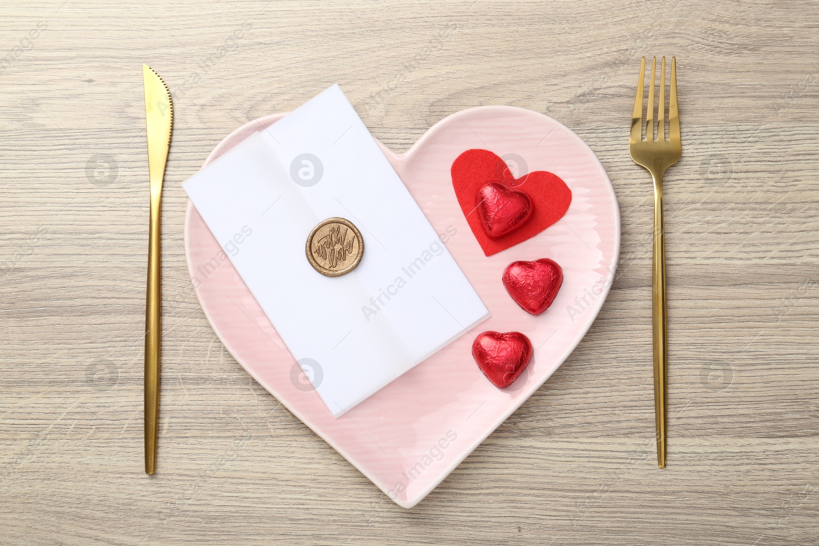 Photo of Romantic place setting with cutlery and heart-shaped plate on wooden table, top view. Valentine's day celebration