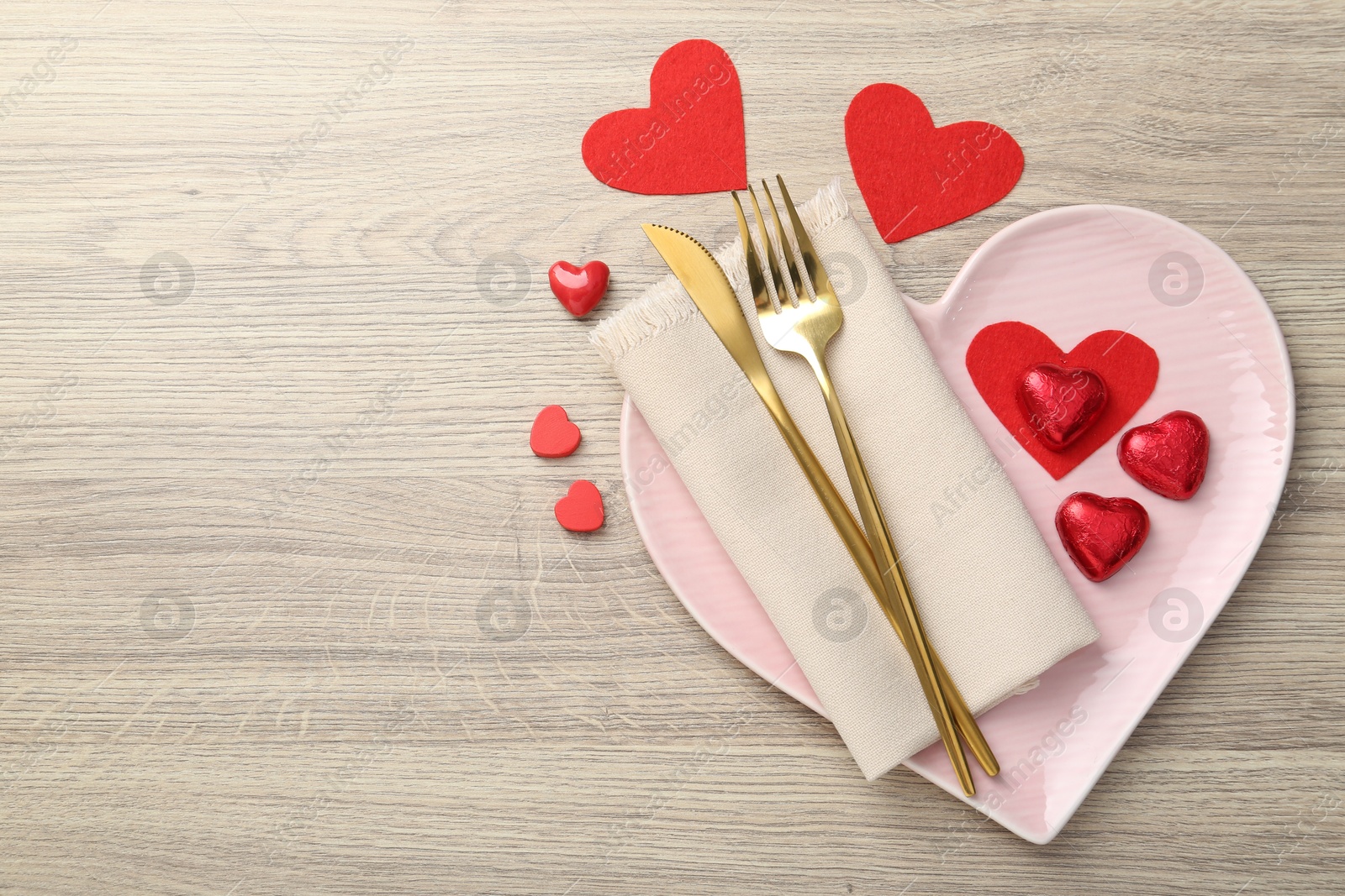 Photo of Romantic place setting with cutlery and heart-shaped plate on wooden table, top view. Valentine's day celebration