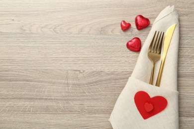 Photo of Romantic place setting with cutlery and hearts on wooden table, top view. Valentine's day celebration