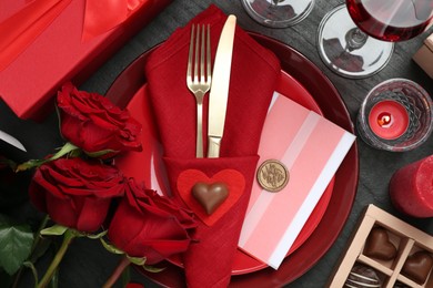 Photo of Romantic place setting with red roses on black table, flat lay. Valentine's day celebration