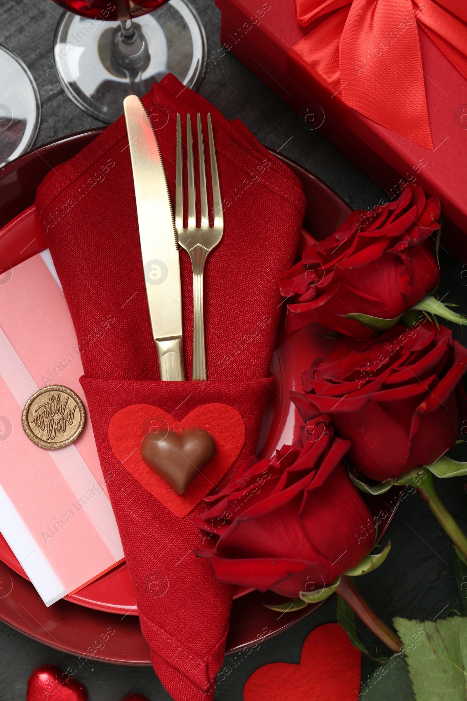 Photo of Romantic place setting with red roses on black table, flat lay. Valentine's day celebration