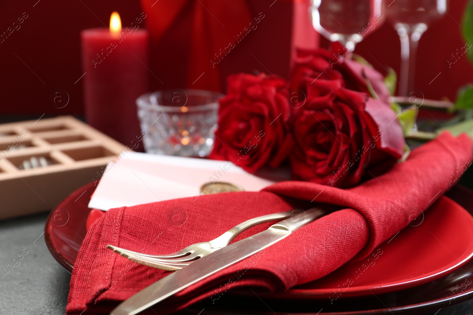 Photo of Romantic place setting with red roses on grey table, closeup. Valentine's day celebration