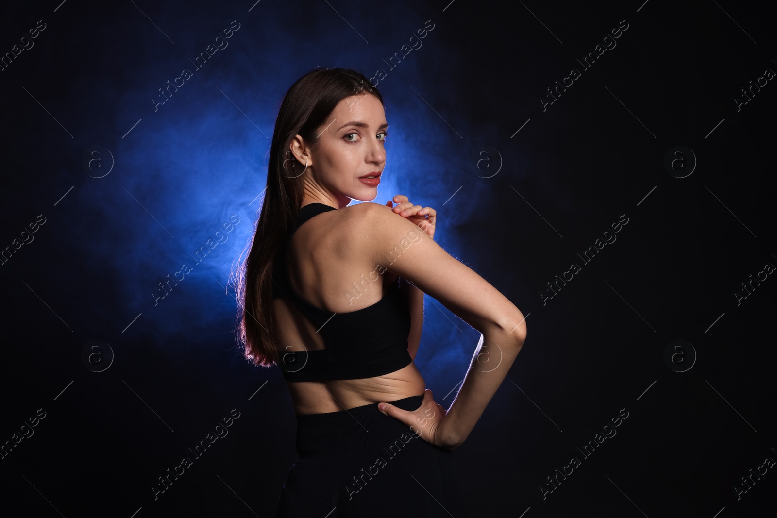 Photo of Beautiful woman in stylish sportswear on dark background with color light and smoke