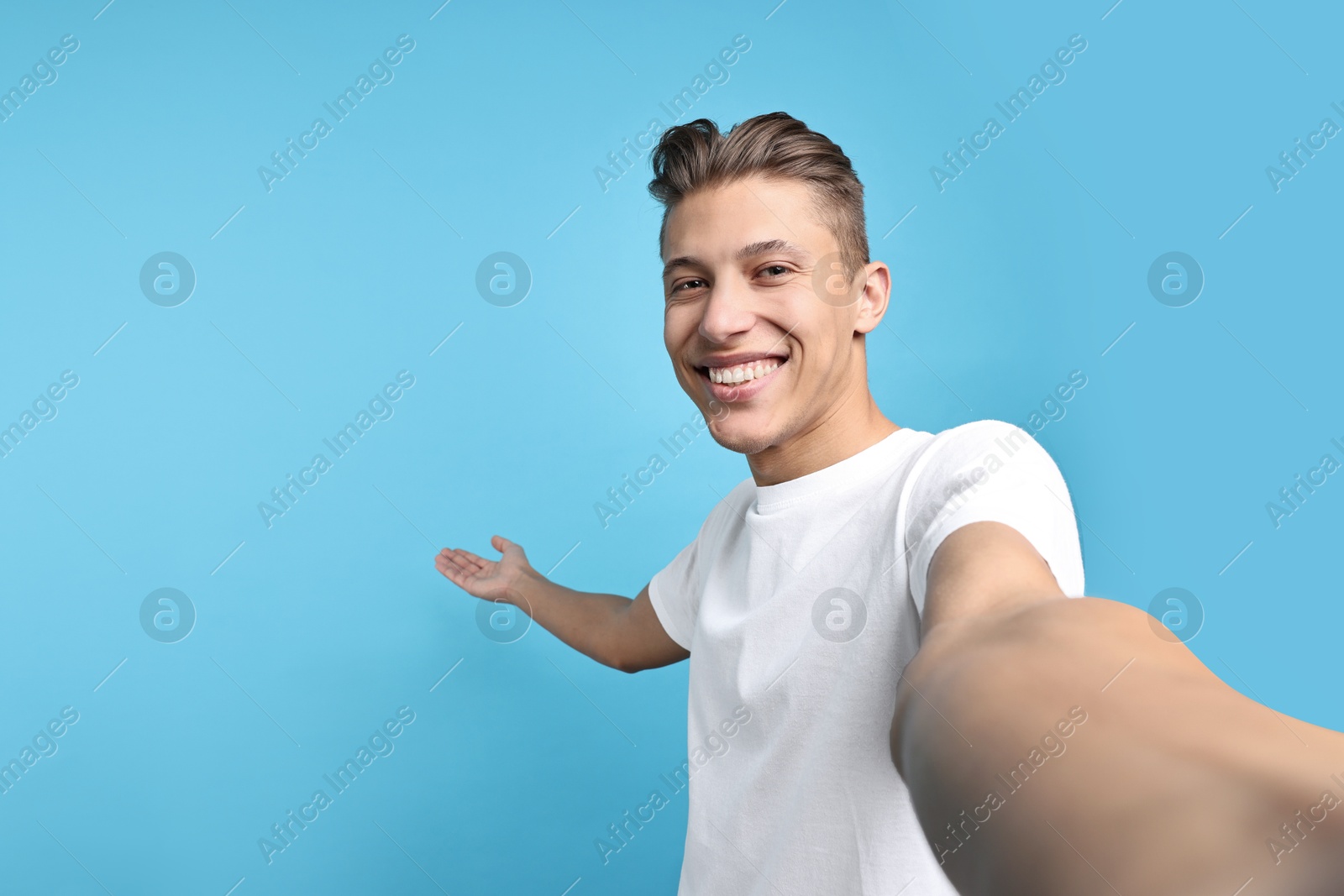 Photo of Happy man taking selfie and welcoming friends or guests on light blue background. Space for text