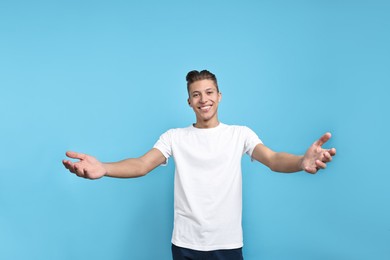 Photo of Happy man welcoming friends or guests on light blue background