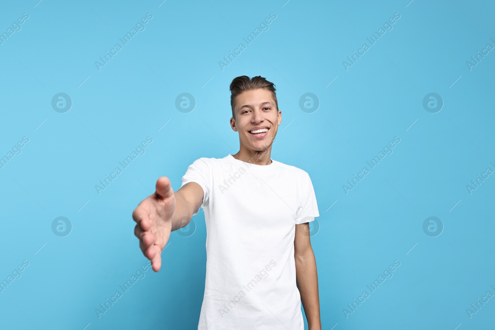 Photo of Happy man welcoming friends or guests on light blue background