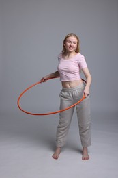 Photo of Beautiful young woman exercising with hula hoop on grey background