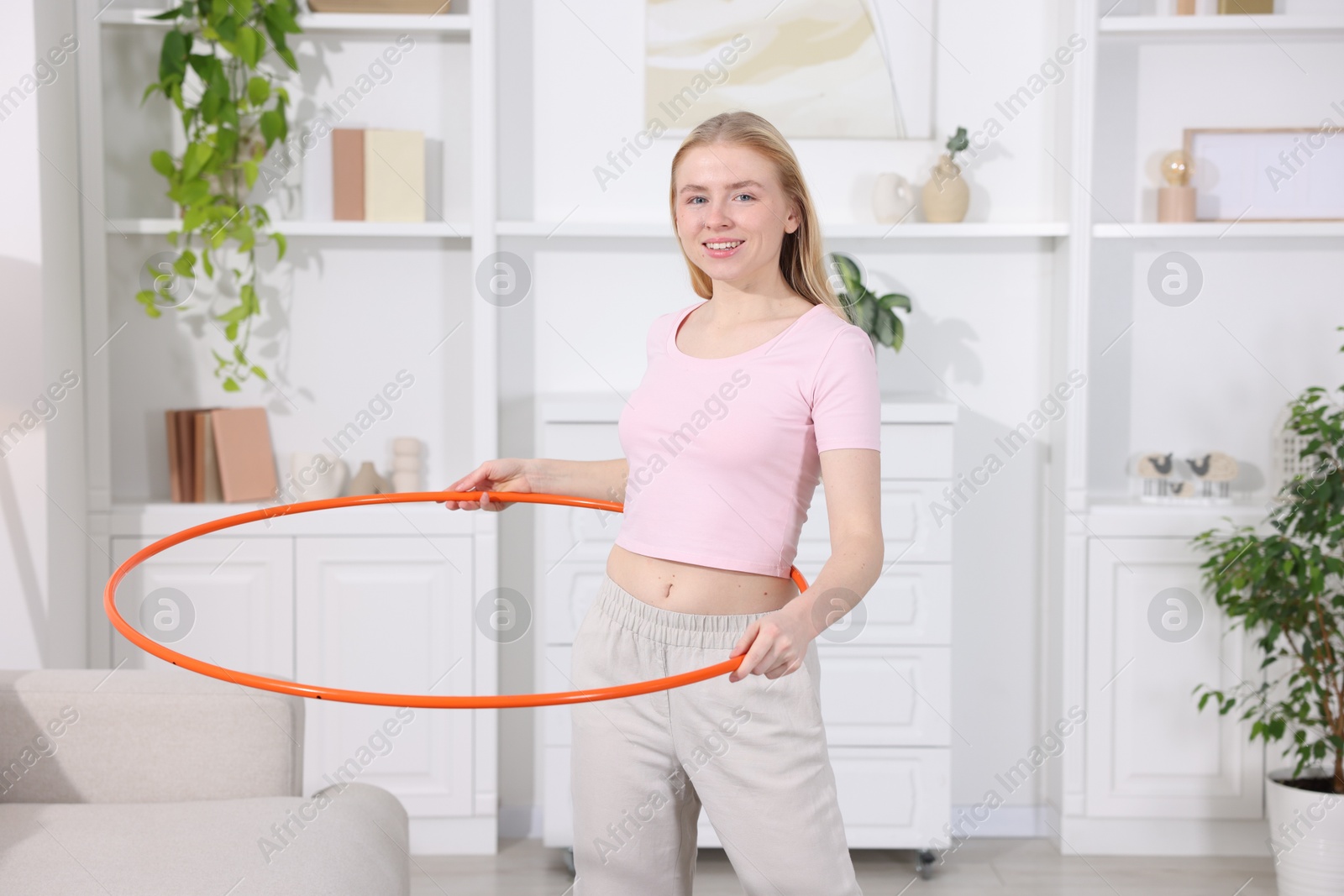 Photo of Beautiful young woman exercising with hula hoop at home