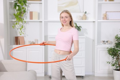 Photo of Beautiful young woman exercising with hula hoop at home