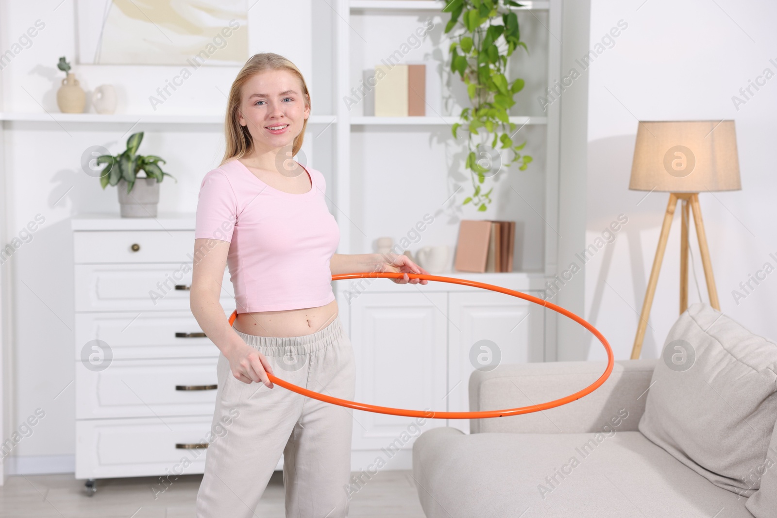 Photo of Beautiful young woman exercising with hula hoop at home