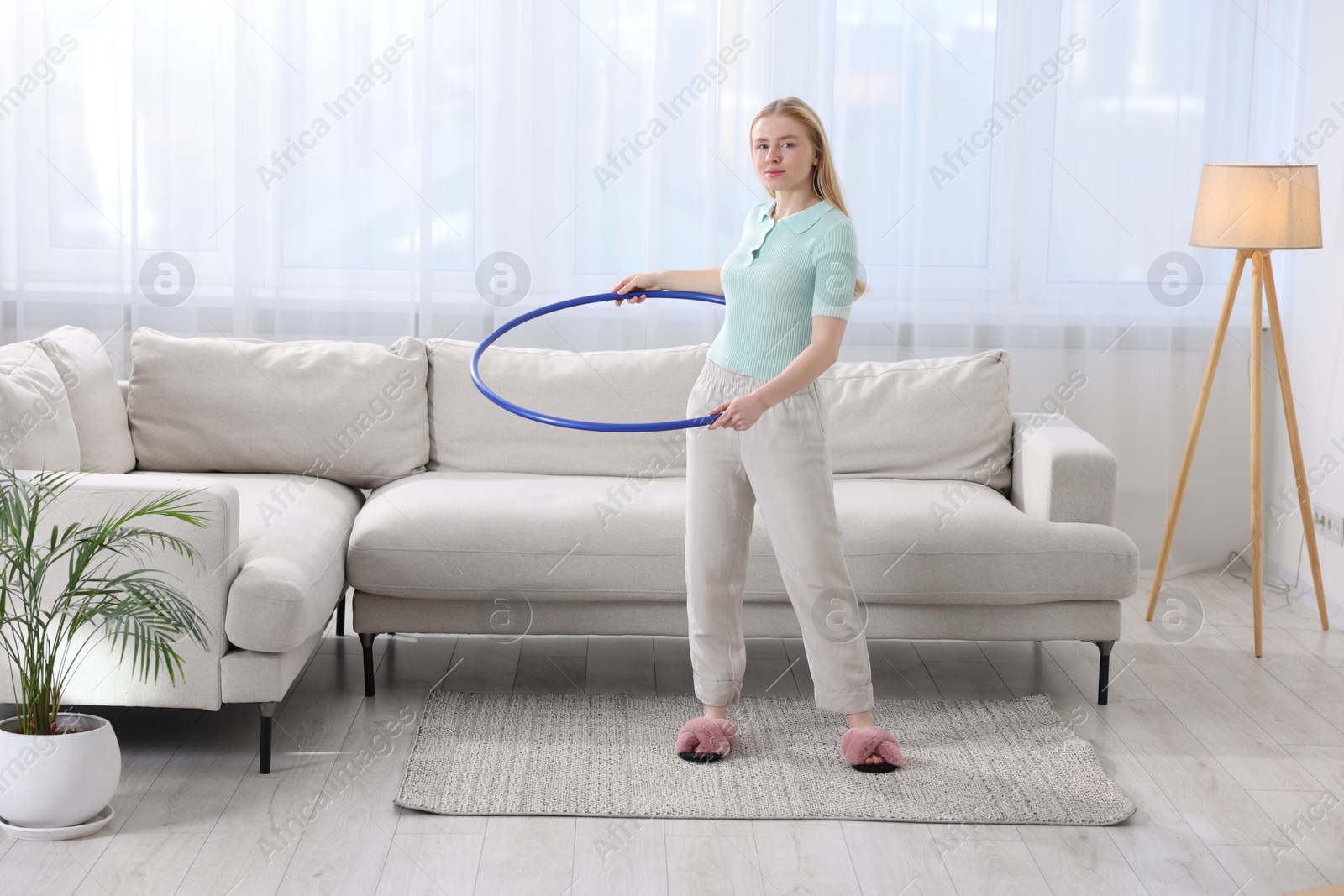 Photo of Beautiful young woman exercising with hula hoop at home