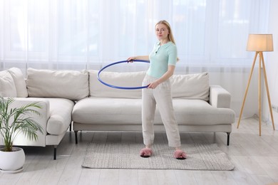 Photo of Beautiful young woman exercising with hula hoop at home