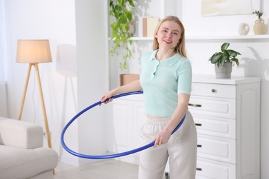 Photo of Beautiful young woman exercising with hula hoop at home