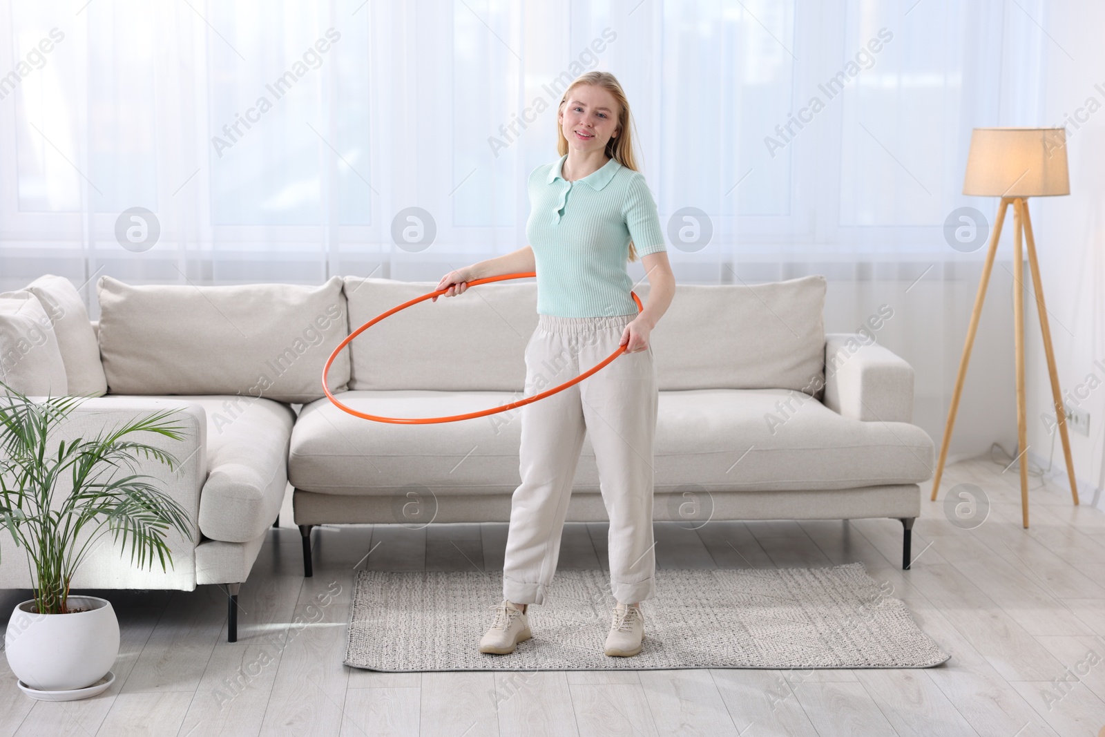 Photo of Beautiful young woman exercising with hula hoop at home