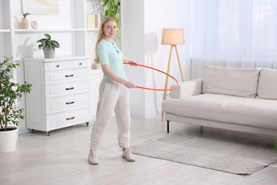 Photo of Beautiful young woman exercising with hula hoop at home