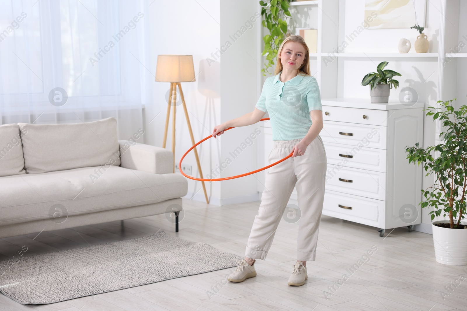 Photo of Beautiful young woman exercising with hula hoop at home