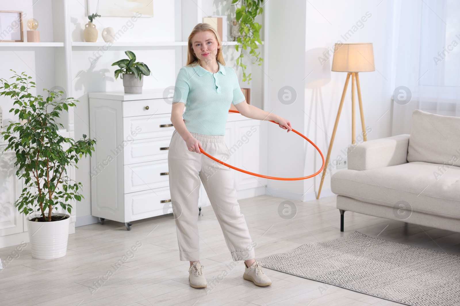 Photo of Beautiful young woman exercising with hula hoop at home