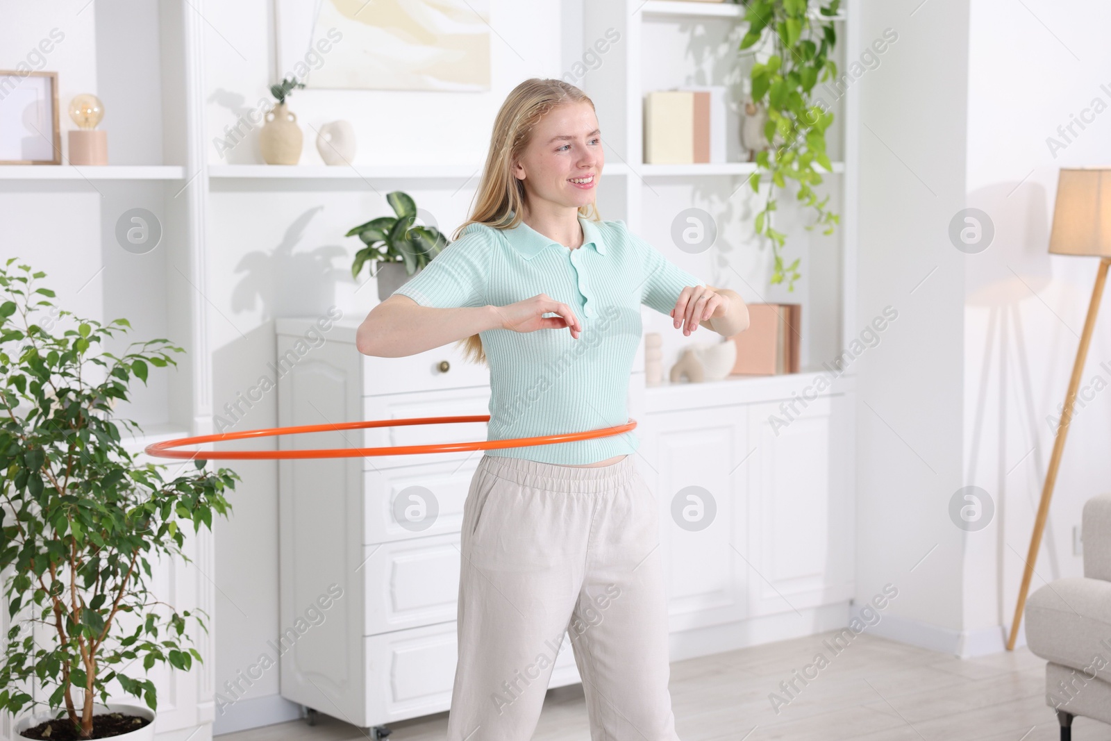 Photo of Beautiful young woman exercising with hula hoop at home