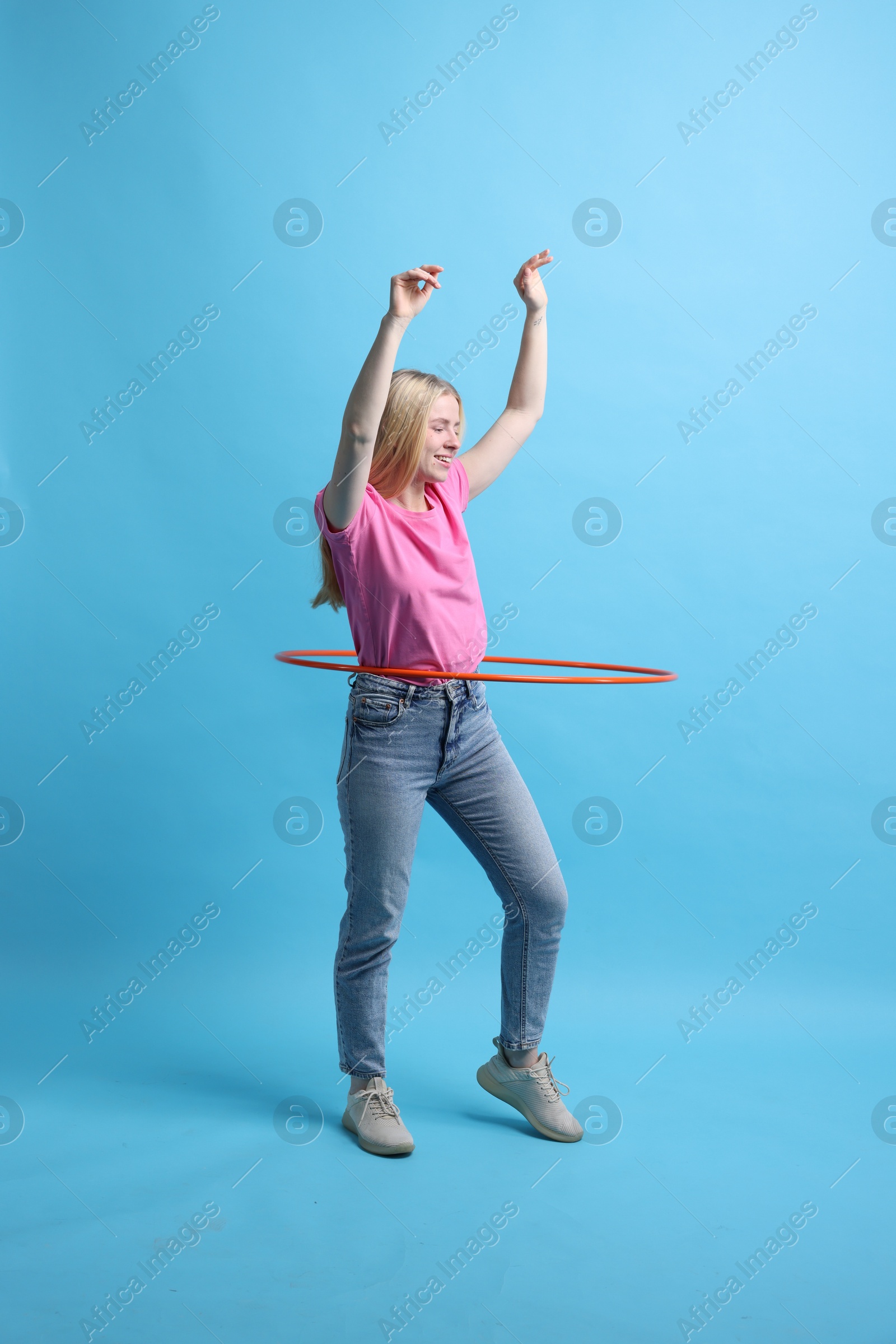 Photo of Beautiful young woman exercising with hula hoop on light blue background