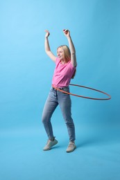 Photo of Beautiful young woman exercising with hula hoop on light blue background