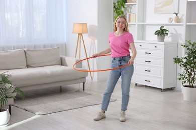 Photo of Beautiful young woman exercising with hula hoop at home