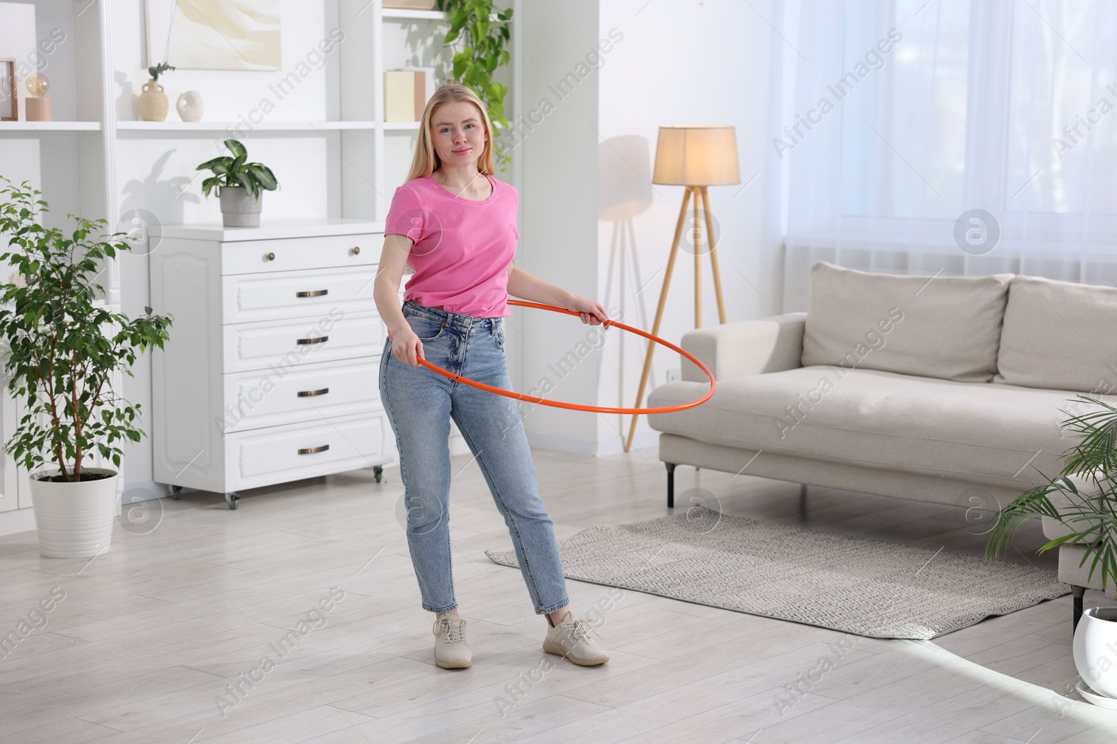 Photo of Beautiful young woman exercising with hula hoop at home