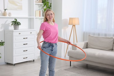 Photo of Beautiful young woman exercising with hula hoop at home