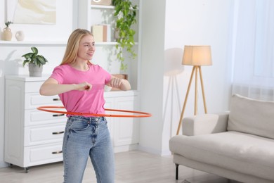 Photo of Beautiful young woman exercising with hula hoop at home