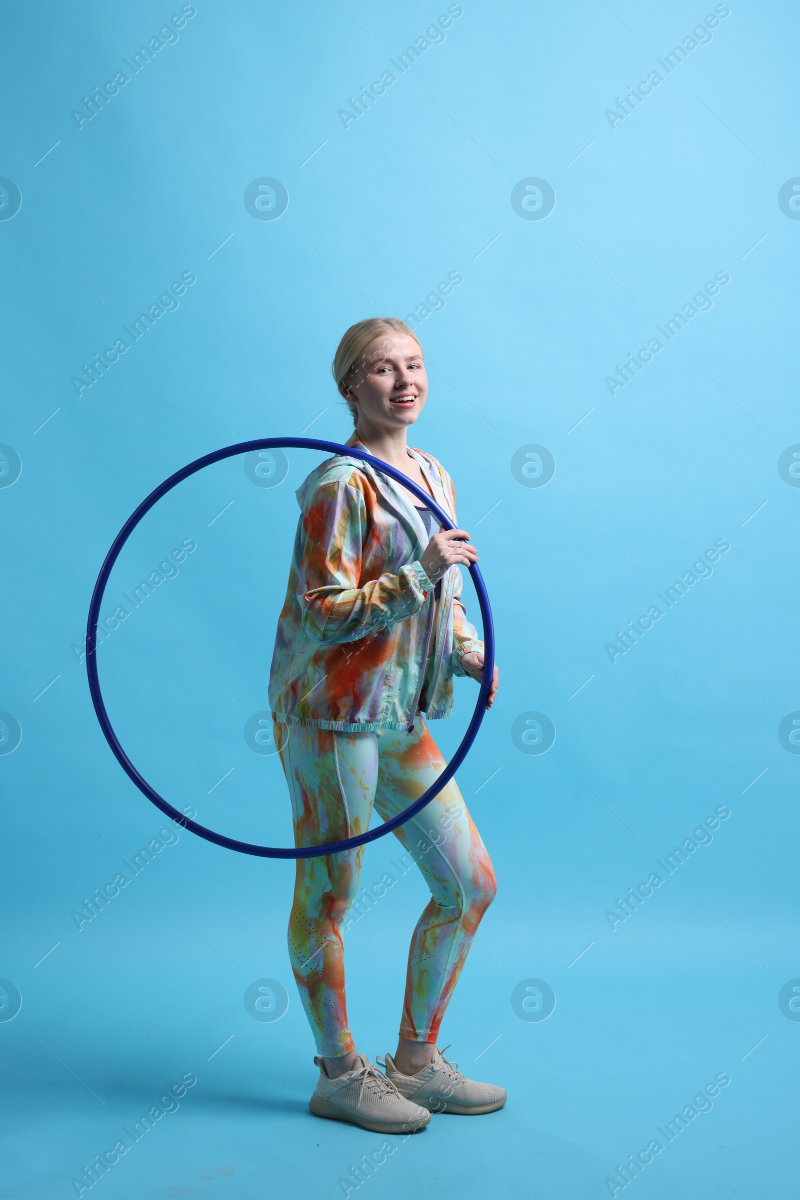 Photo of Beautiful young woman with hula hoop on light blue background