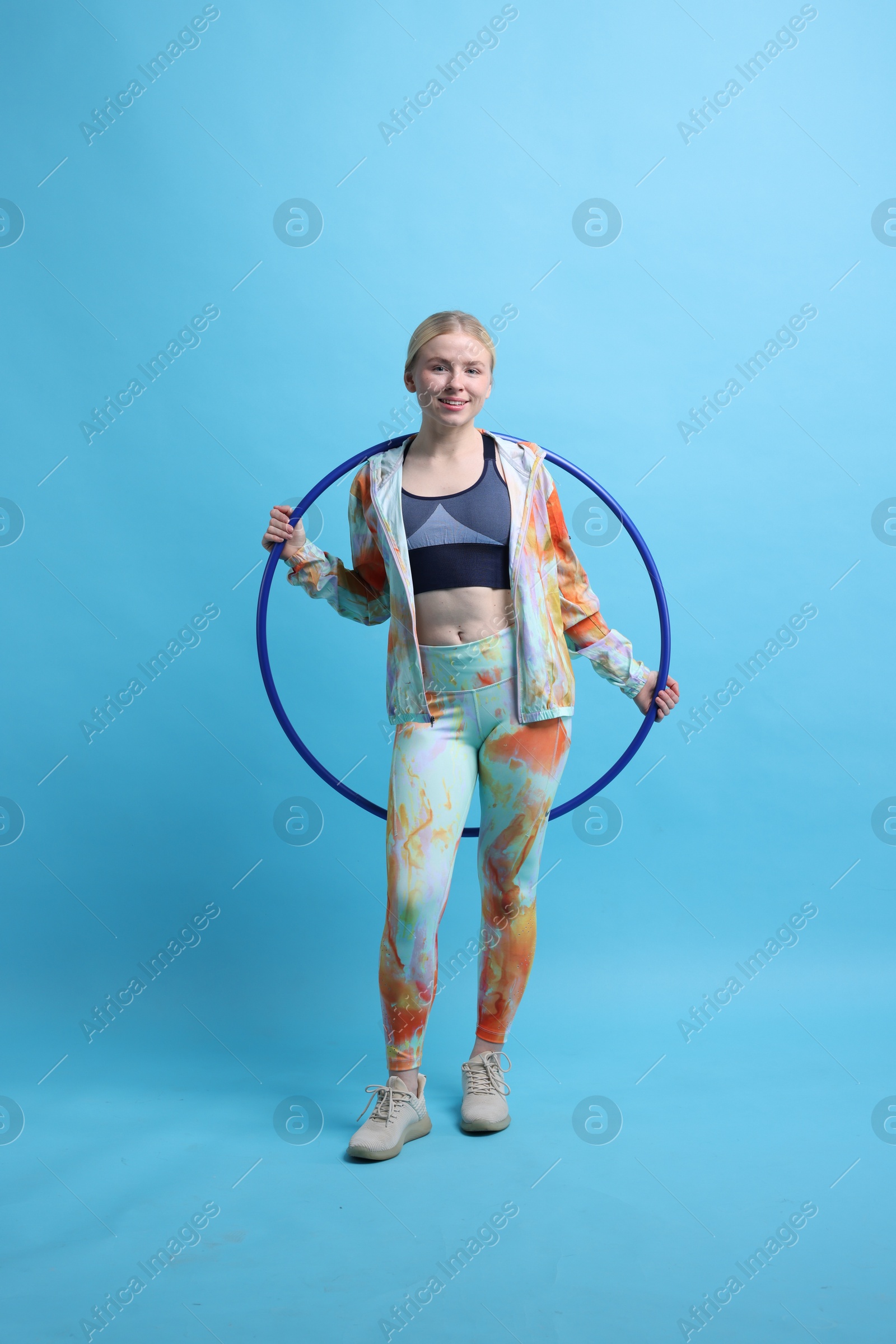 Photo of Beautiful young woman with hula hoop on light blue background