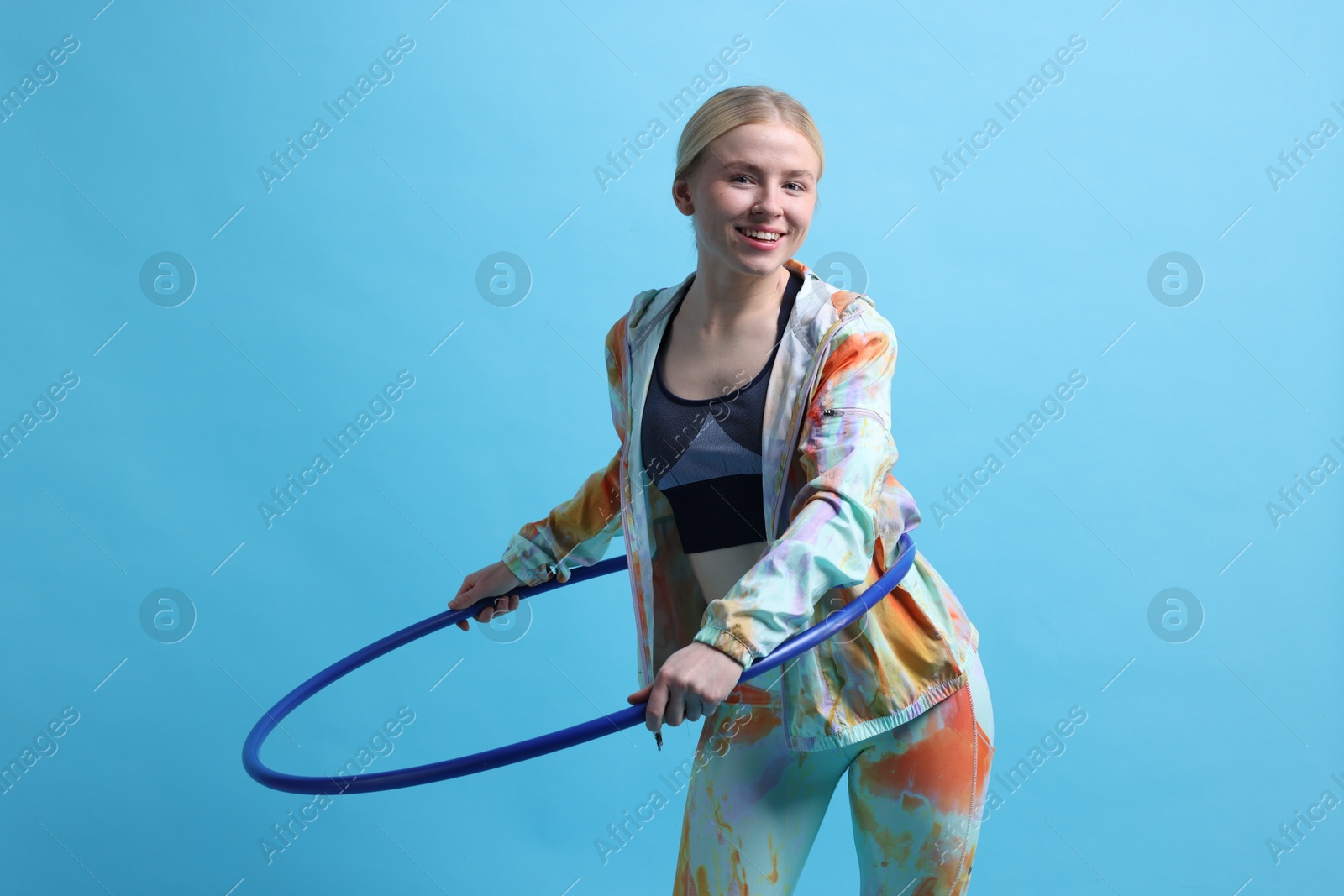 Photo of Beautiful young woman exercising with hula hoop on light blue background