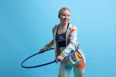 Photo of Beautiful young woman exercising with hula hoop on light blue background