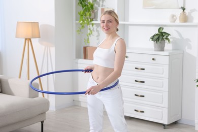 Photo of Beautiful young woman exercising with hula hoop at home