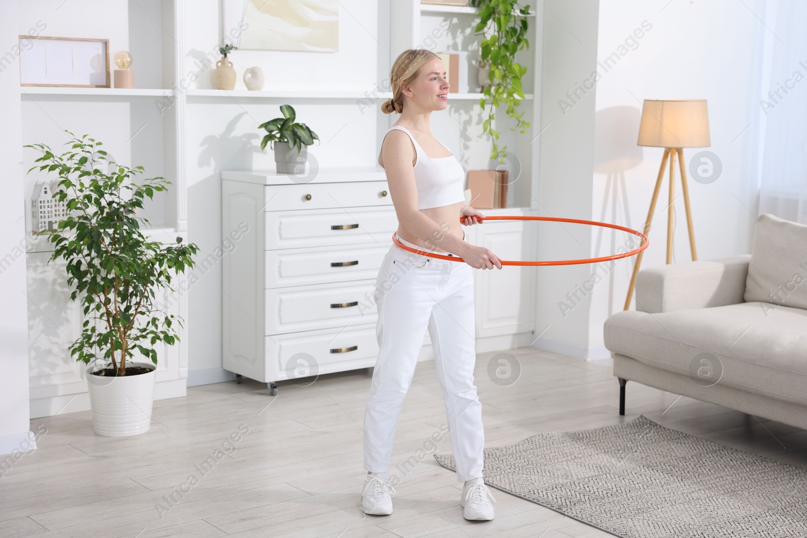 Photo of Beautiful young woman exercising with hula hoop at home