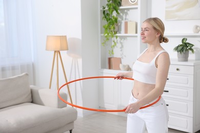 Photo of Beautiful young woman exercising with hula hoop at home