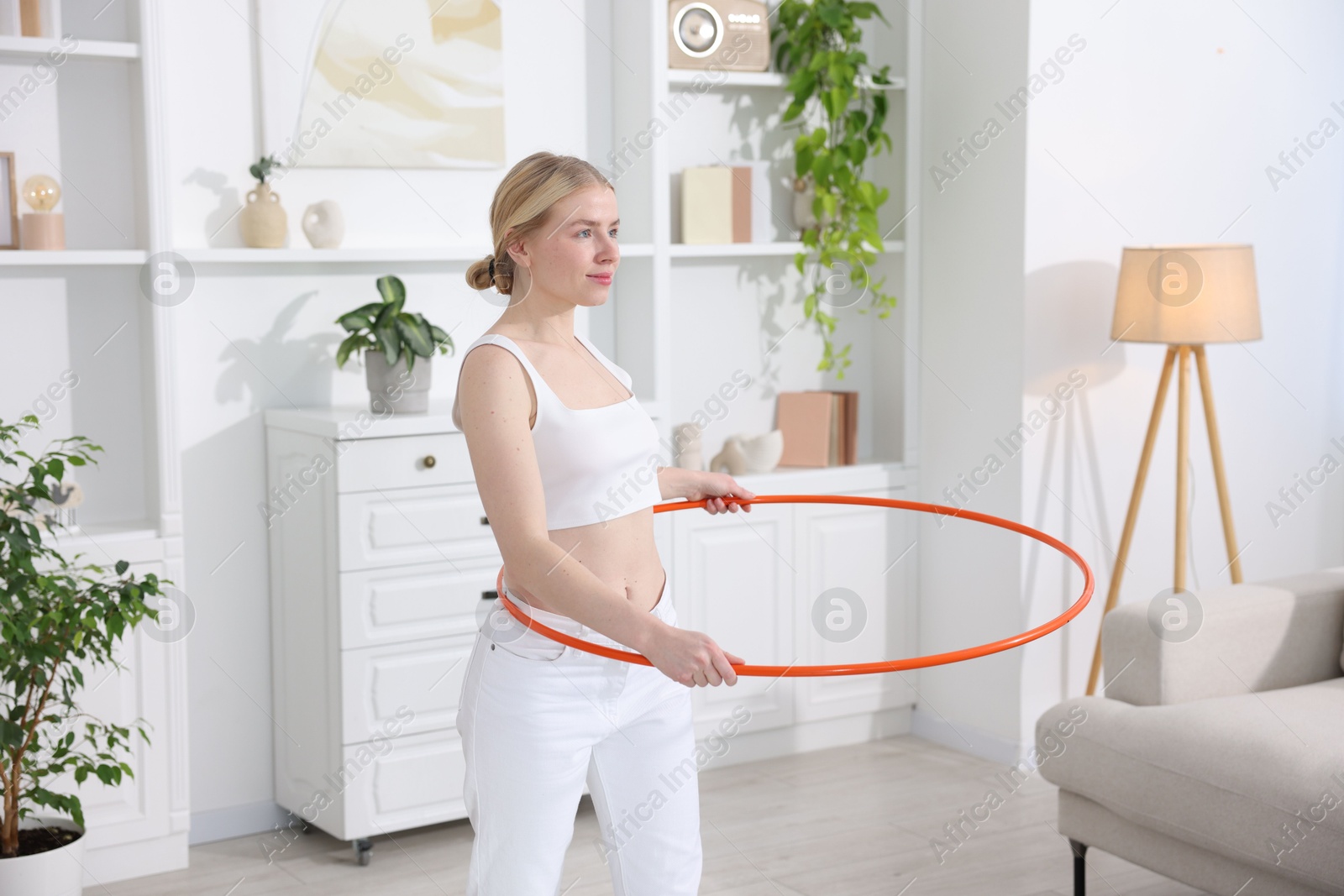 Photo of Beautiful young woman exercising with hula hoop at home