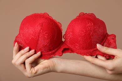 Photo of Woman holding red bra on dark beige background, closeup