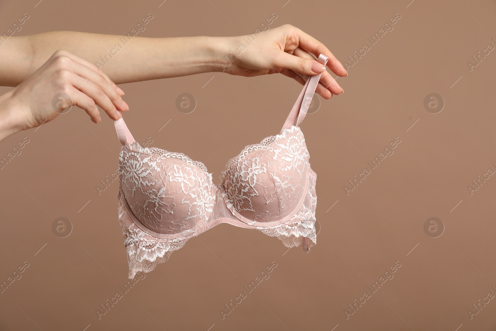 Photo of Woman holding lace bra on dark beige background, closeup. Space for text