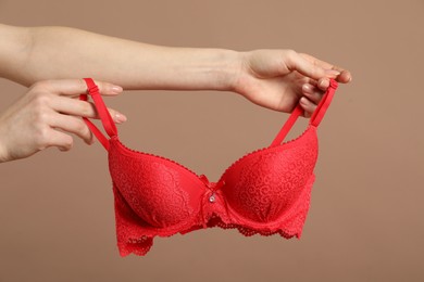 Photo of Woman holding red bra on dark beige background, closeup